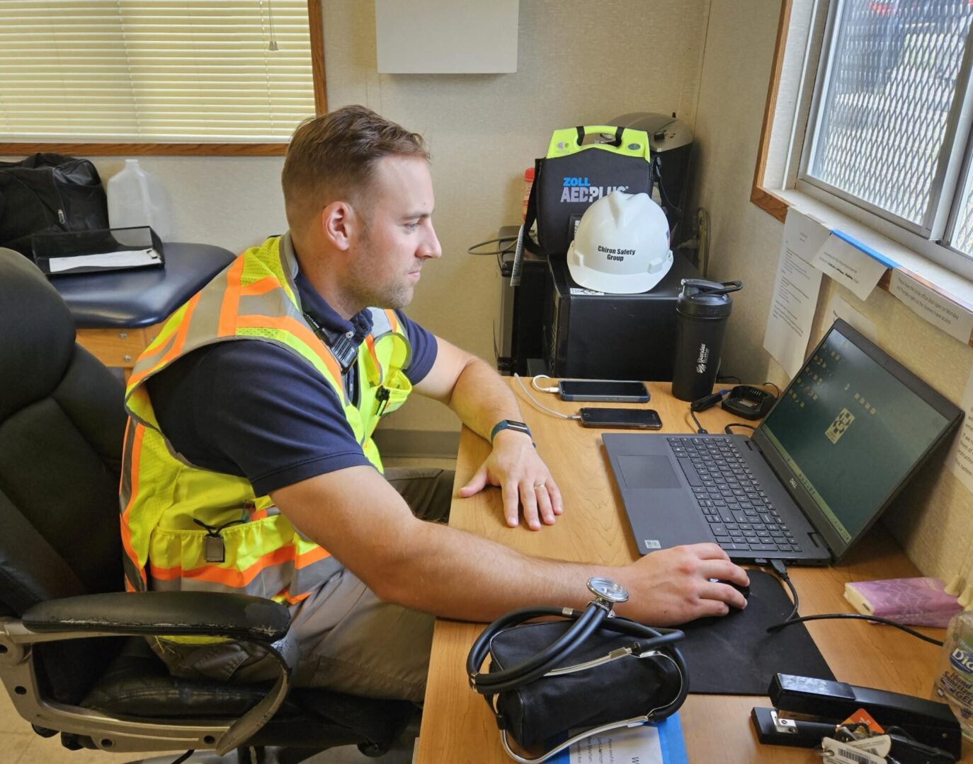 A man in an orange vest is sitting at his desk